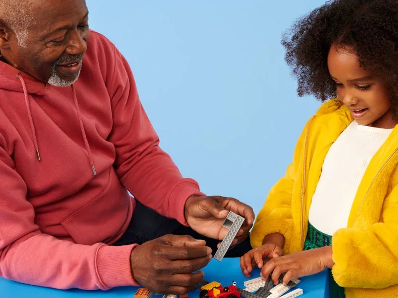 A grandfather and his granddaughter building a LEGO set together at a table