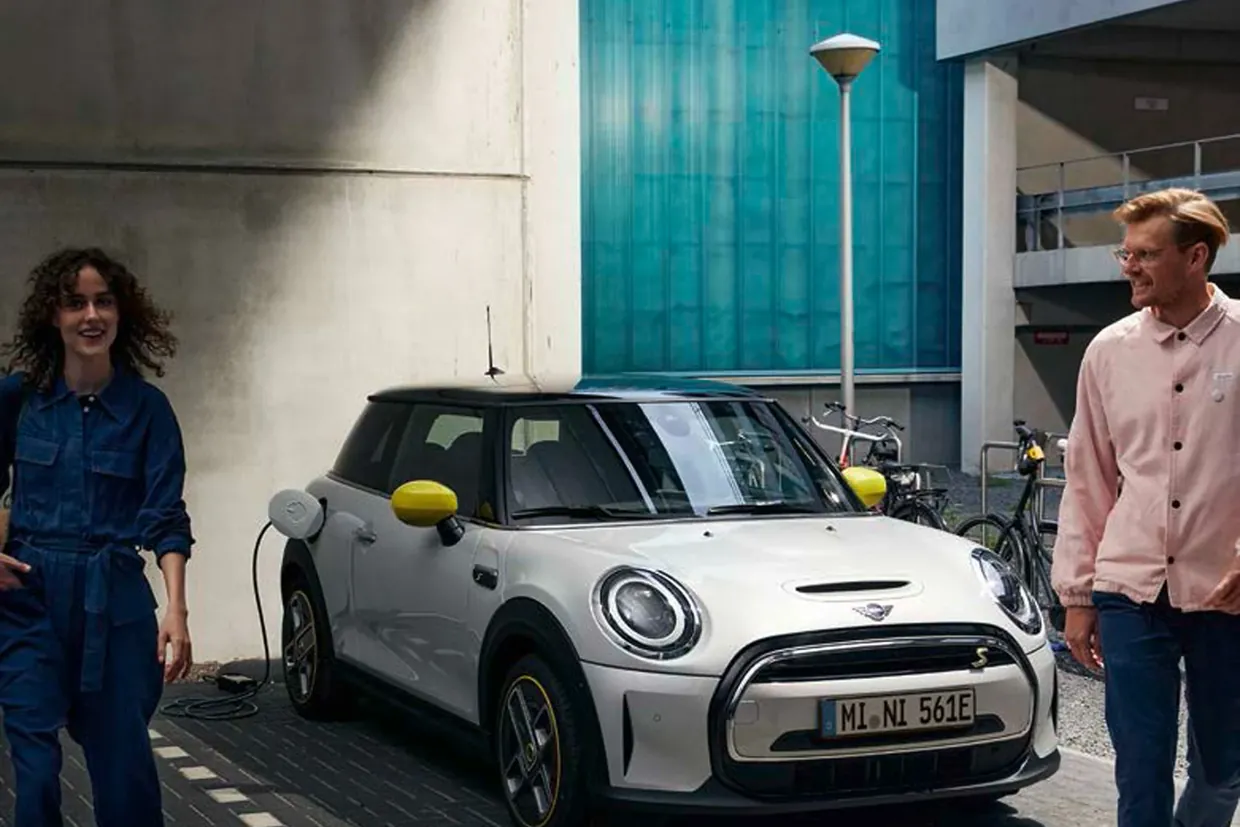 A white MINI Electric charging at a kerbside point while two people walk past