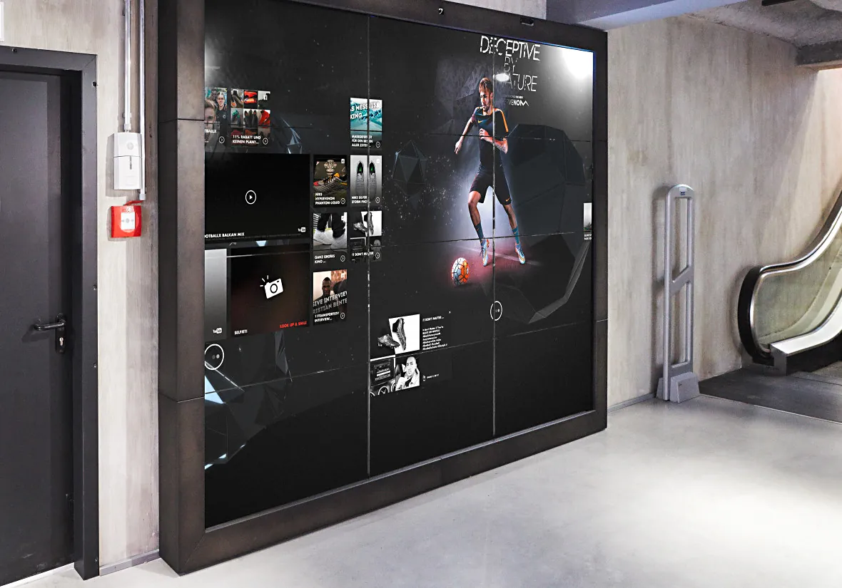 A digital product wall in the Nike football flagship beside the escalator, running player imagery on a dark screen