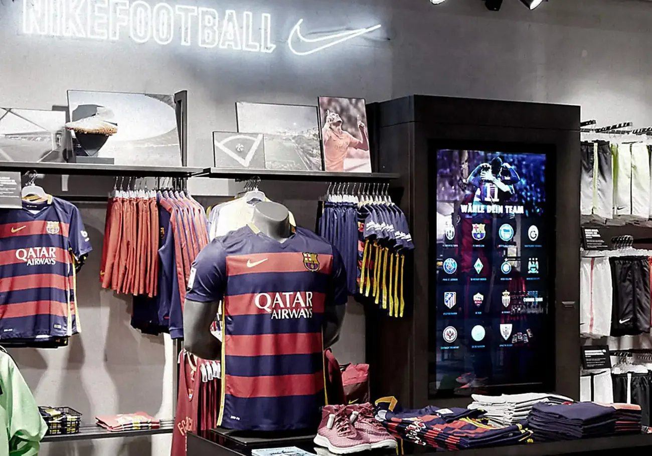 The replica area under the NIKEFOOTBALL sign, club shirts on hangers beside the lit team selector kiosk
