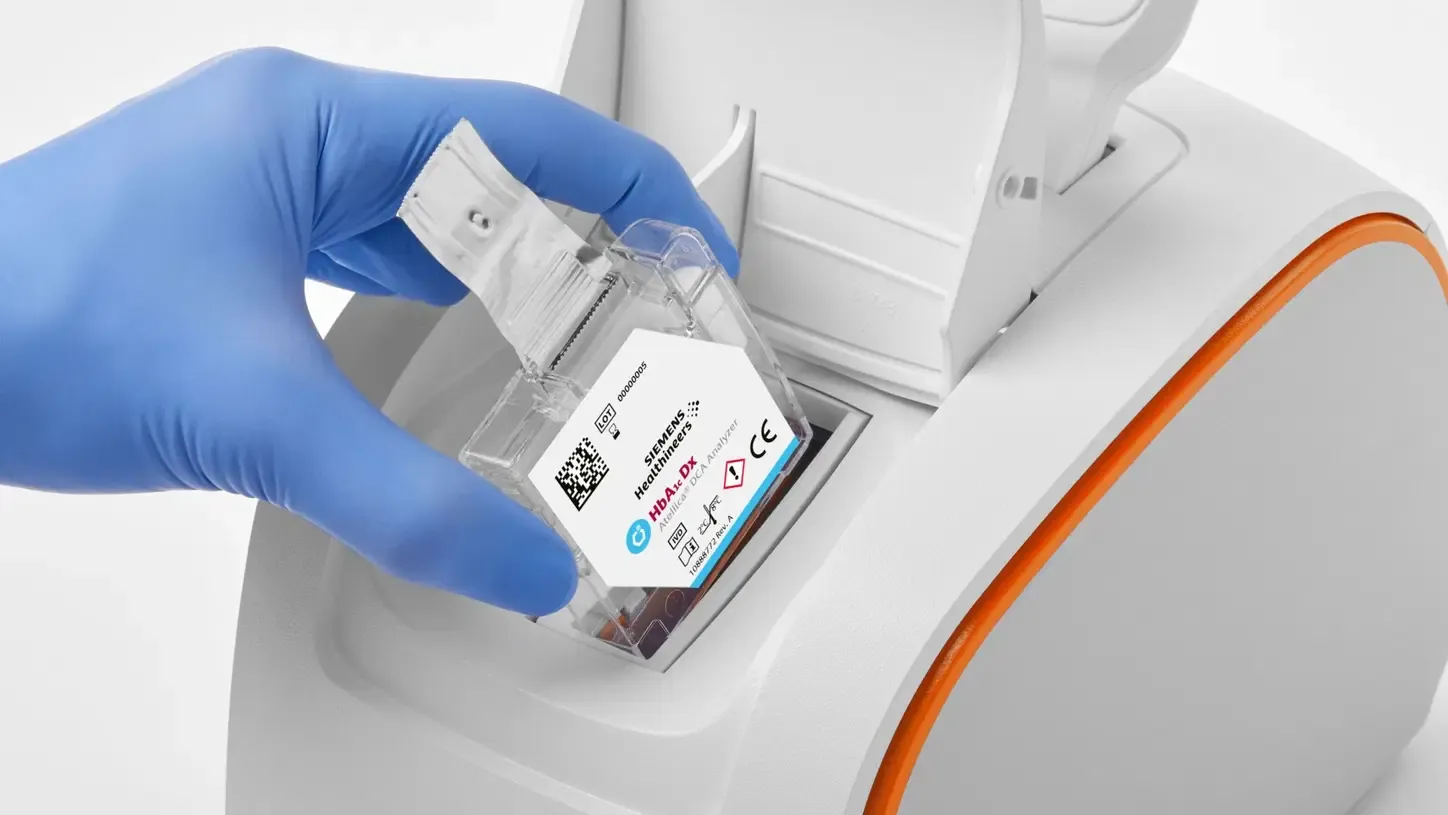 A gloved hand loading a test cartridge into the Atellica DCA analyzer