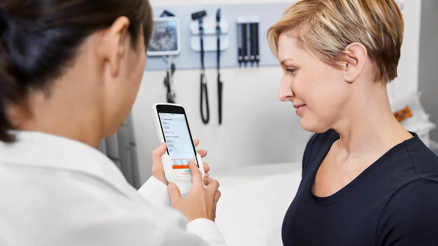 A clinician and a patient reading a result on the handheld Atellica DCA in an exam room